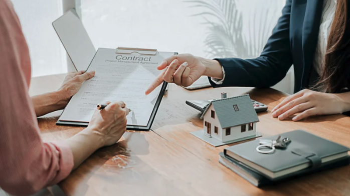 Real estate agent explaining property contract to client with house model and keys on desk
